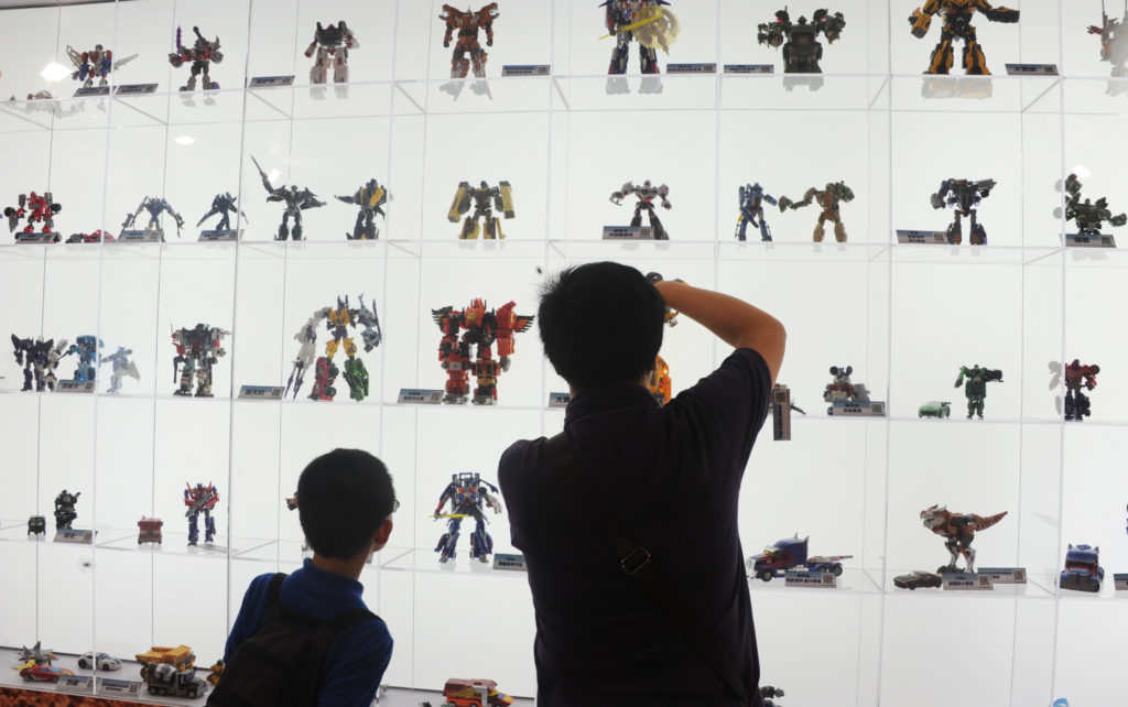 A man and a boy looking at a large collection of Transformers toys placed in a glass toy cabinet.