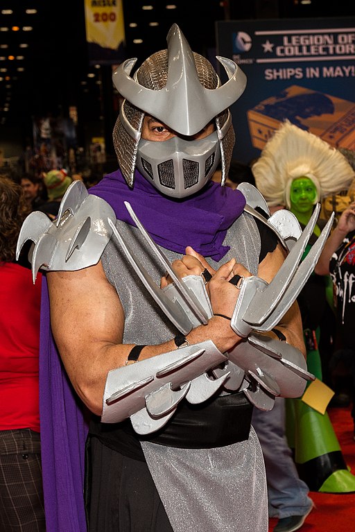 A man in a Shredder costume in full hand, body, and head armor with a purple cape