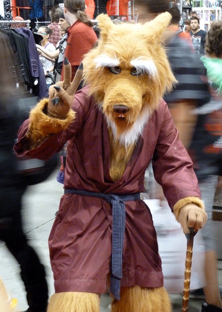 A man in a Splinter, the human-rat, costume doing a peace sign while holding his cane