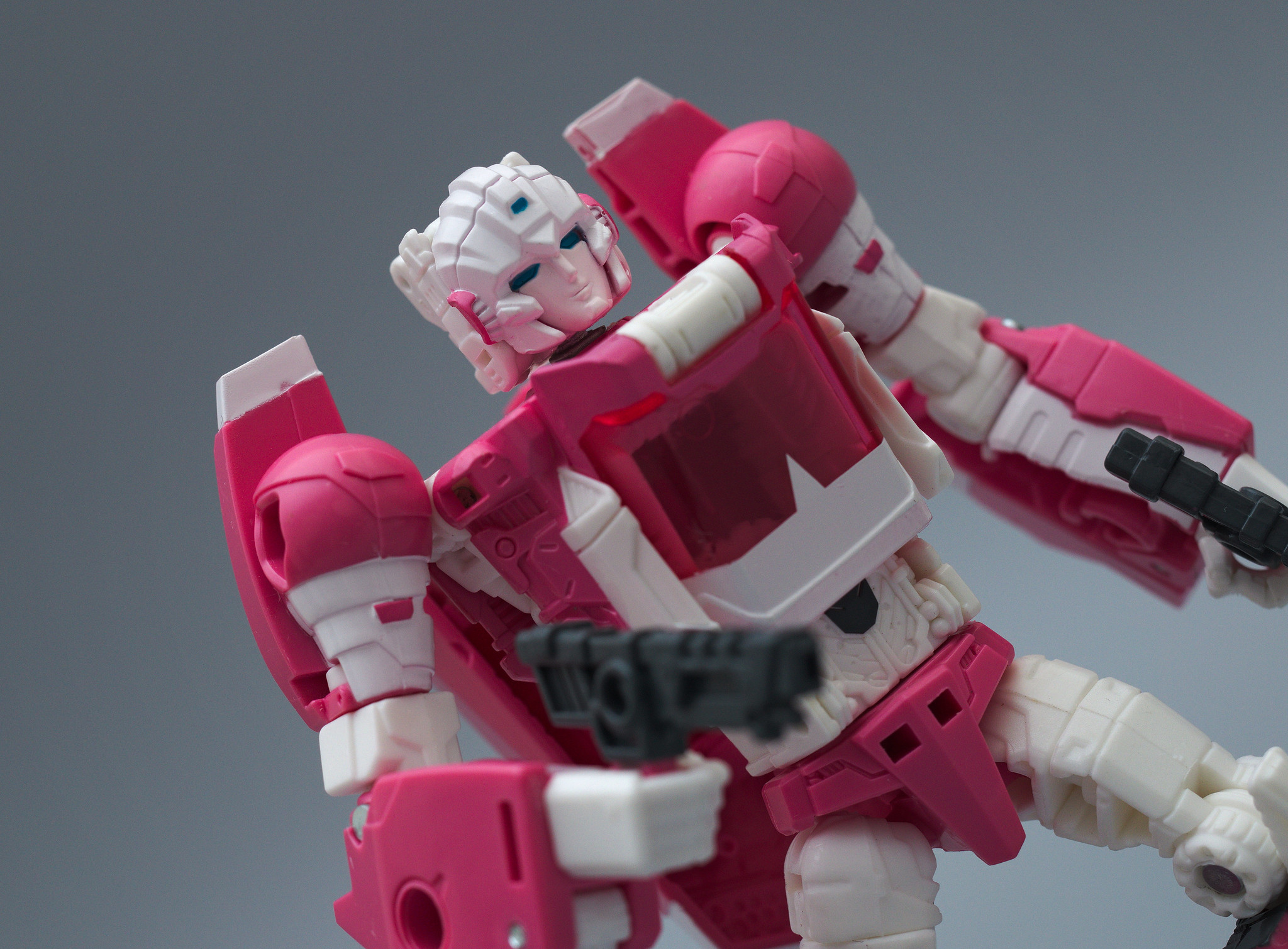 Pink and white Autobot Arcee holding black guns in her right and left hands