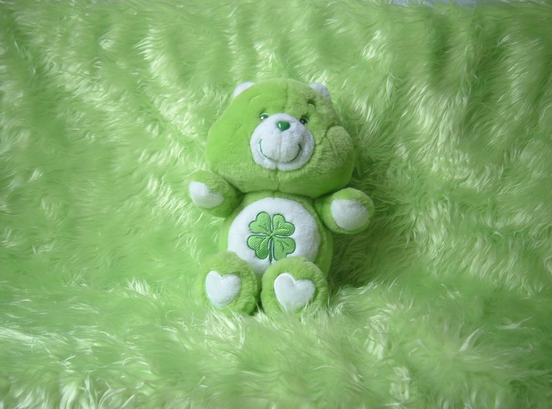 Good Luck Bear, the green Care Bear with a four-leaf clover on his tummy, with green faux feather background