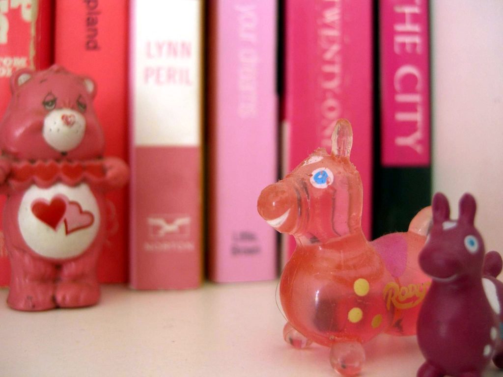 Love-a-lot Bear, a Pink Care Bear, carries a red heart with a pink outline and a pink heart with a yellow outline intertwined on her tummy.