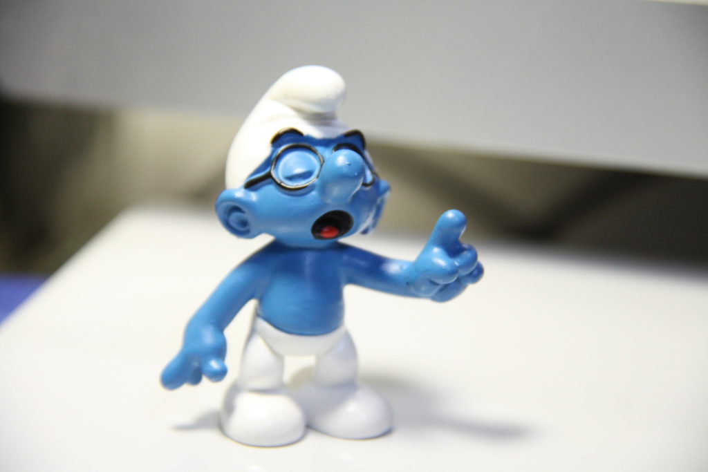 Brainy Smurf in white hat and pants and round glasses, eyes closed while finger pointing in front