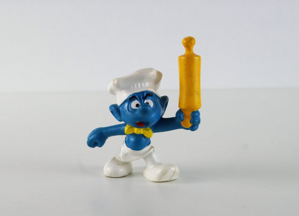 Chef Smurf wears an all-white chef's hat, pants, apron