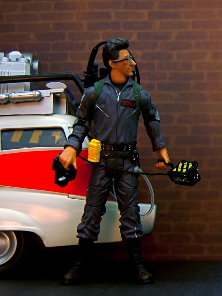 Egon Spengler toy in full gear, standing beside the Ectomobile