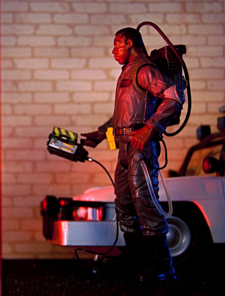 Winston Zeddemore toy figure wearing a proton pack while standing beside a vehicle