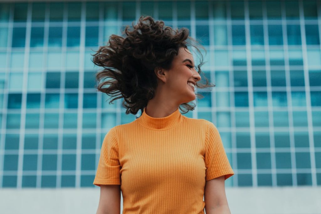 A smiling woman with a big hair wearing an orange turtle neck shirt