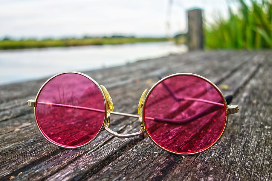 A round colored sunglasses on top of a wood beside a lake