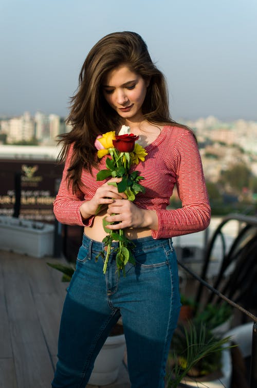 A woman wearing a high waist jeans while holding five roses in different colors