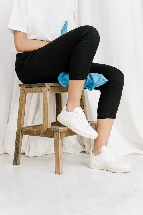 A person wearing a black leggings while sitting on a wooden chair
