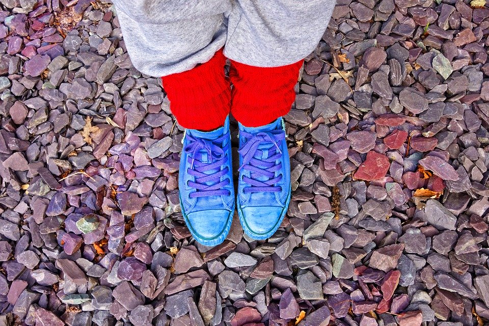 A person’s feet in blue shoes and red leg warmers stepping on a stone-filled floor