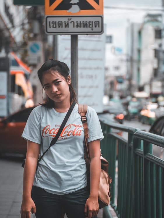 A woman standing in a sidewalk wearing a shirt with metallic Coca-Cola print