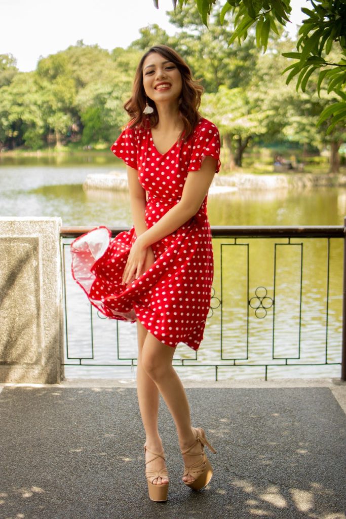 A smiling woman wearing a red dress with white polka dots design