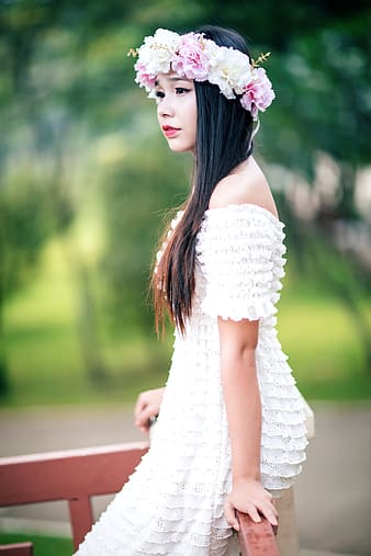 A woman wearing a flower crown and a white off-shoulder dress in ruffles