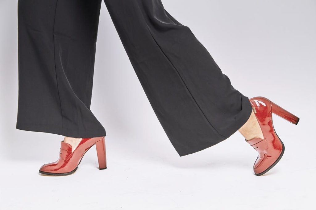 A person wearing a black wide leg black pants and a red high heels 