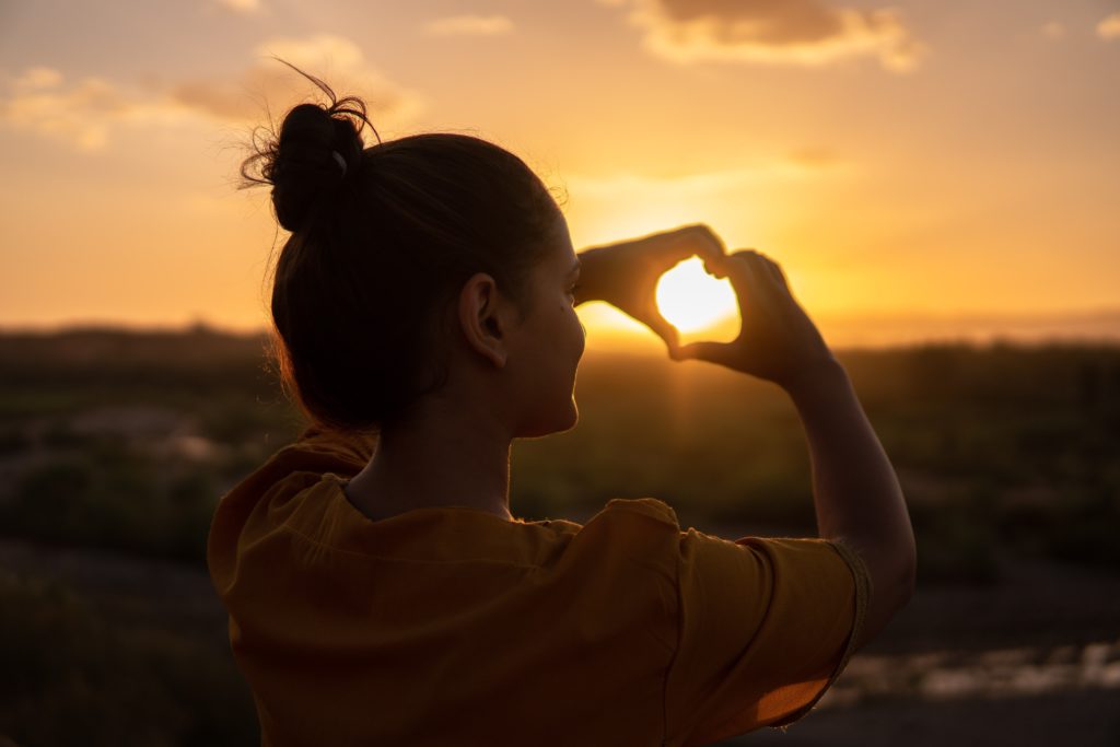 woman doing a heart sign in sunset